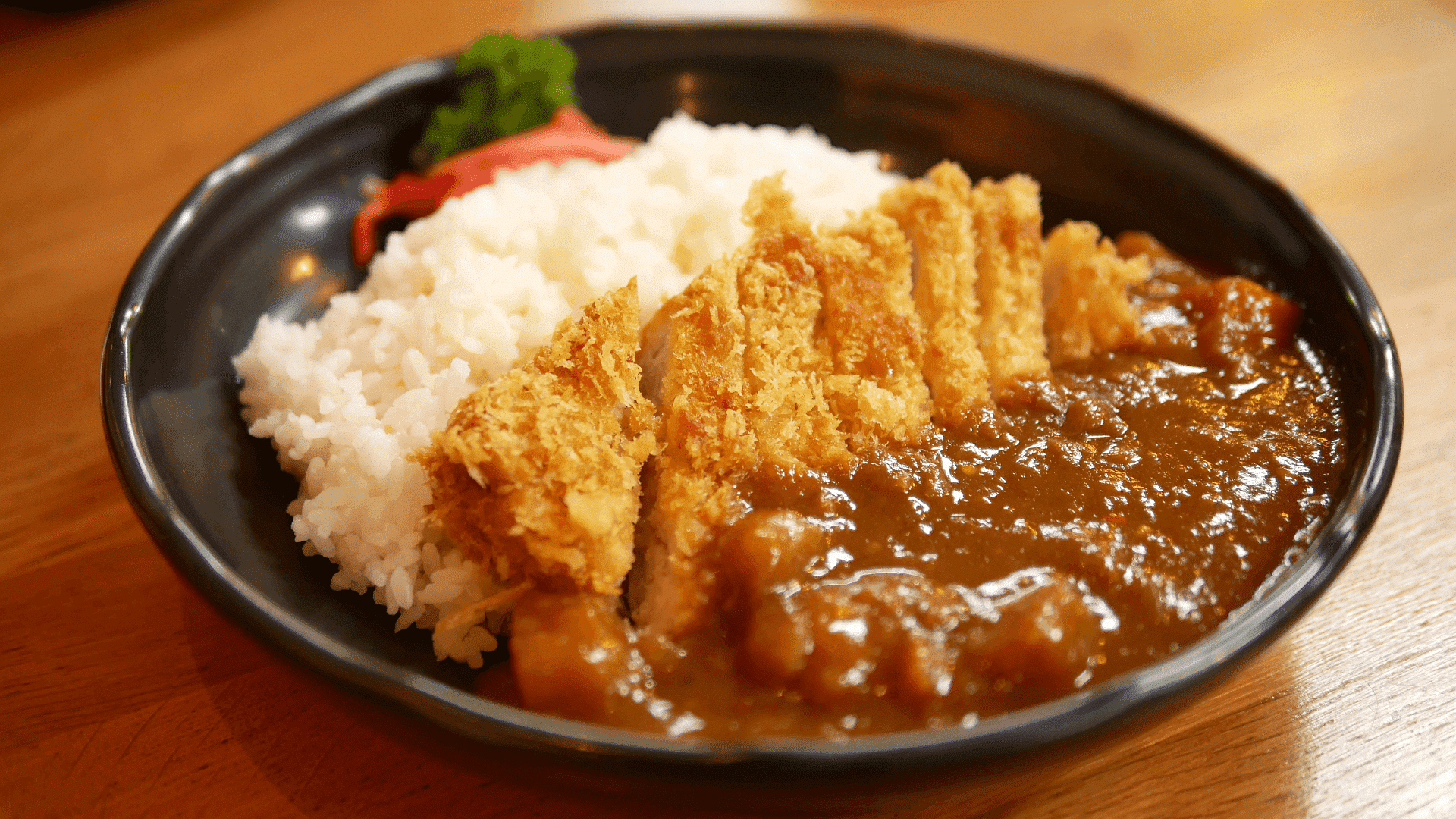 Plate of Japanese curry rice with crispy breaded chicken, garnished with pickled ginger and parsley.