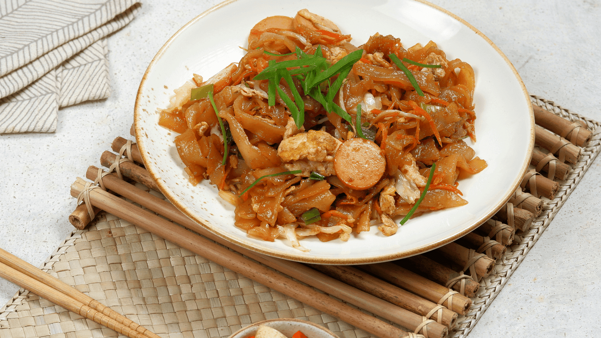 Plate of stir-fried rice noodles with vegetables and sausage, garnished with fresh green onions.