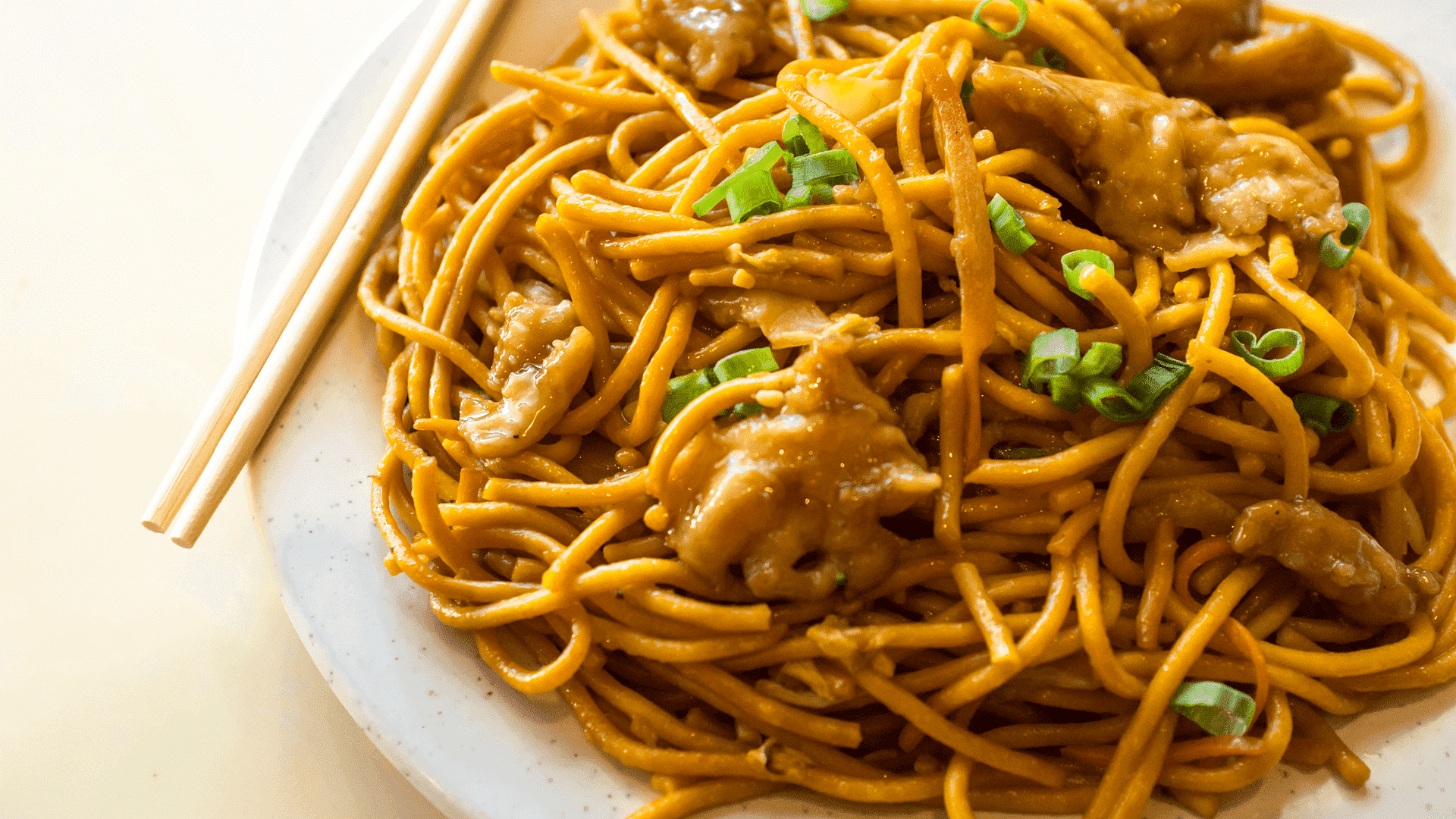 Plate of chow mein with vegetables and chopsticks on the side.